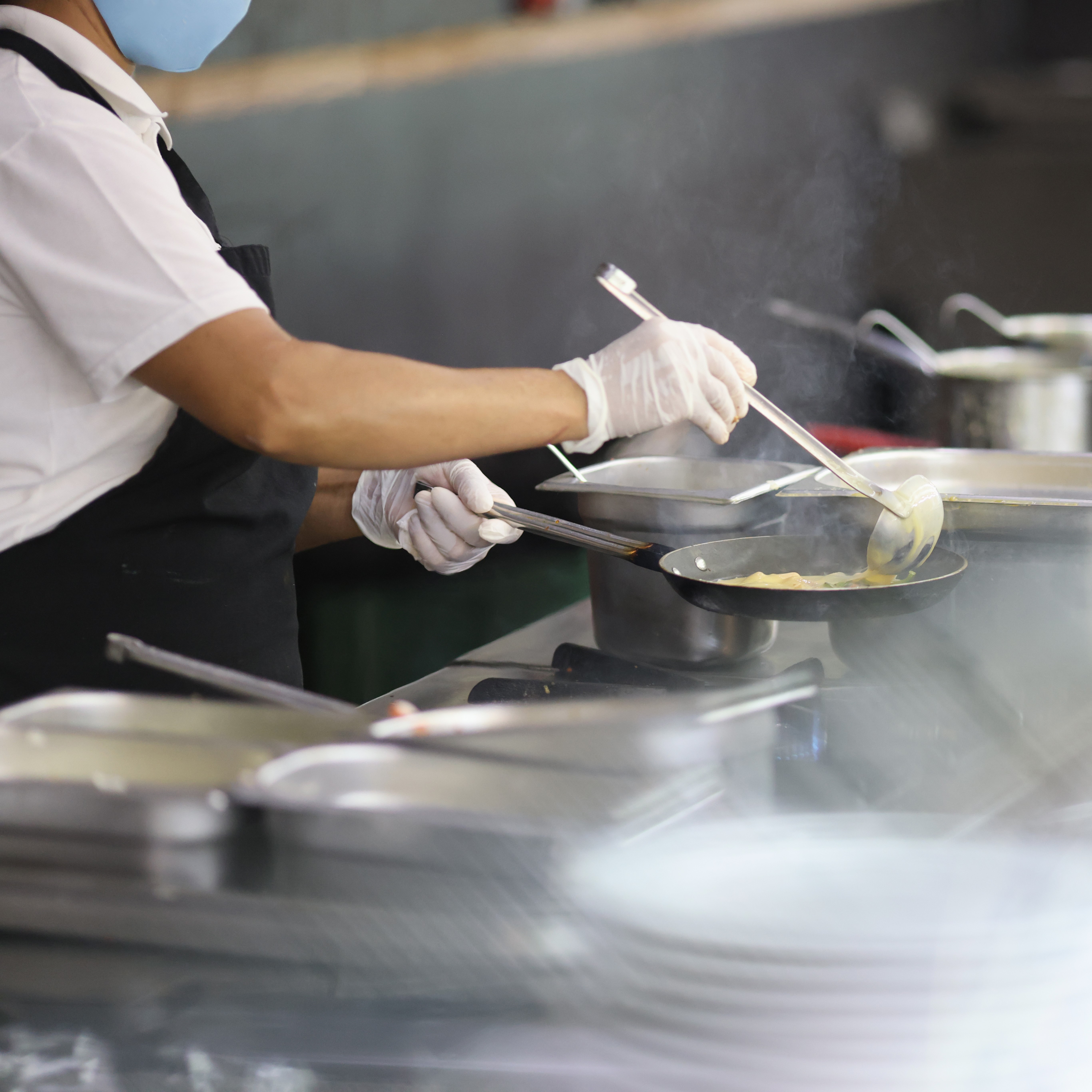 Cook prepares food in frying pan in kitchen