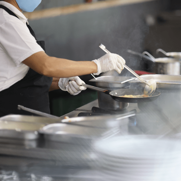 Cook prepares food in frying pan in kitchen