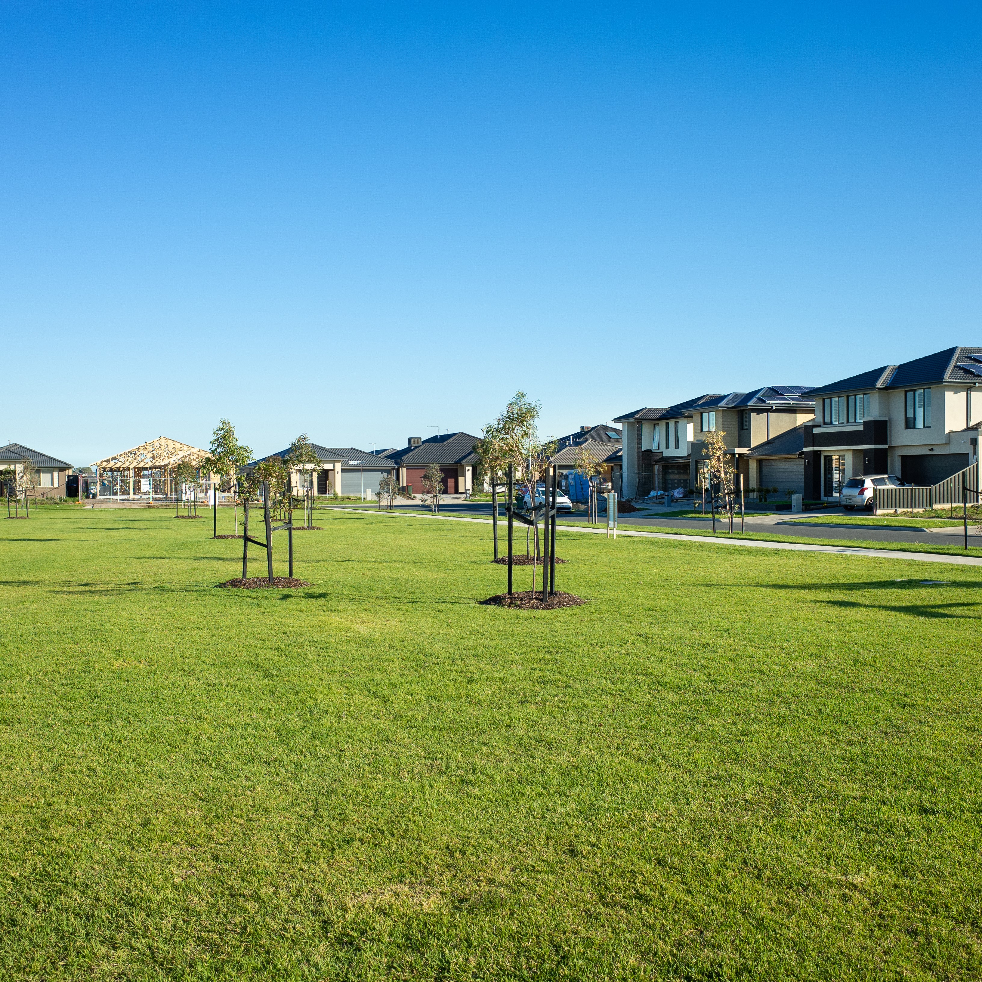 A public park with green lawn/grass and young trees surrounded by new residential houses/Australian homes in a Melbourne's suburb. Tarneit, VIC Australia. Background texture of a
 suburban park.