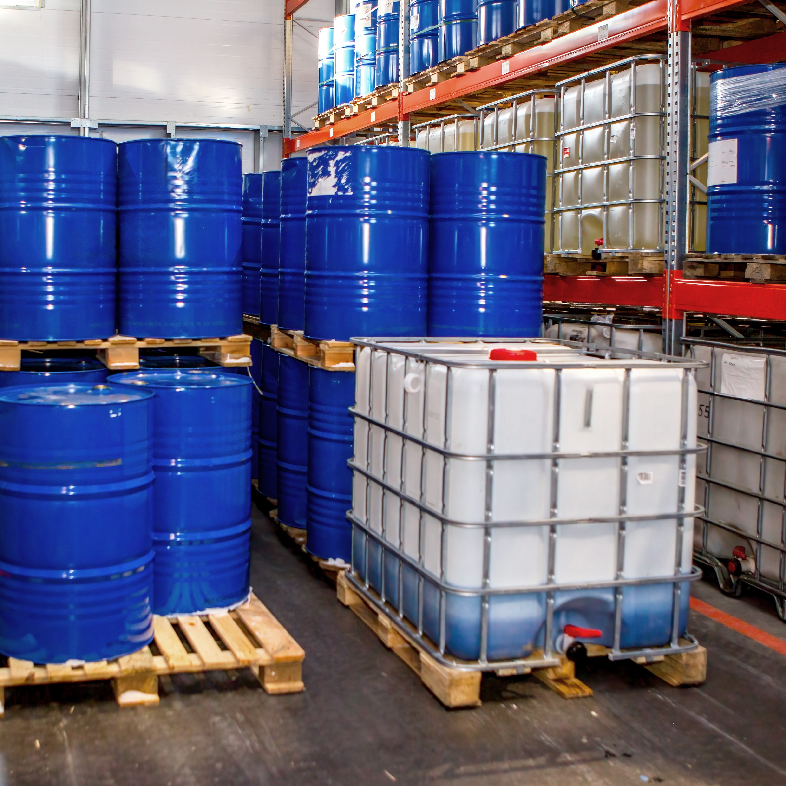 Plastic and metal barrels inside warehouse. Storage chemical products. IBC container with blue liquid. Chemical warehouse inside industrial building. Multi-tiered racks for storing barrels in hangar