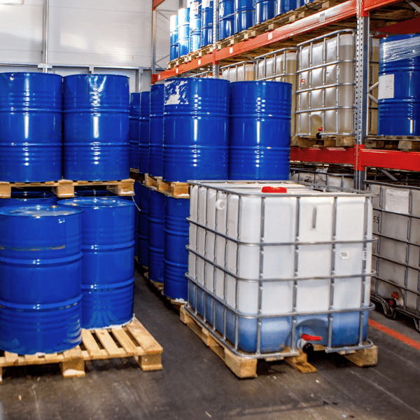 Plastic and metal barrels inside warehouse. Storage chemical products. IBC container with blue liquid. Chemical warehouse inside industrial building. Multi-tiered racks for storing barrels in hangar